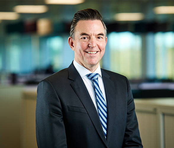 a man with short black hair smiling in a black suit.