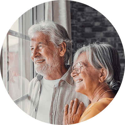 A close up of an elderly couple smiling whilst looking out the window.