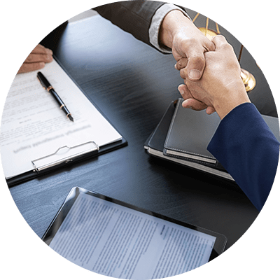 A close up of two men in suits shaking hands across a desk with documents and and ipad on there.