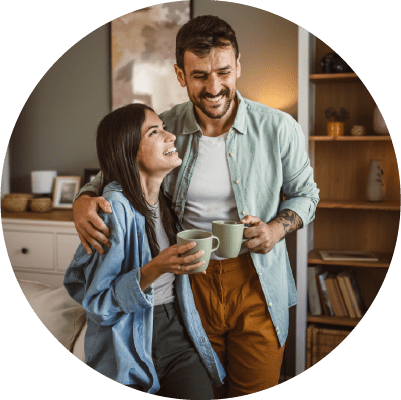 A couple hugging and smiling whilst drinking a coffee together.
