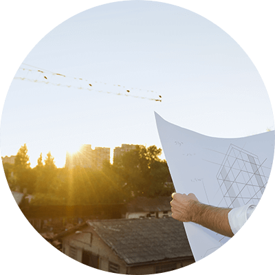 A long shot of a man holding blueprints looking at a view.