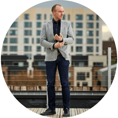 A man stood looking into the distance wearing a grey blazer and blue jeans in front of a skyline.