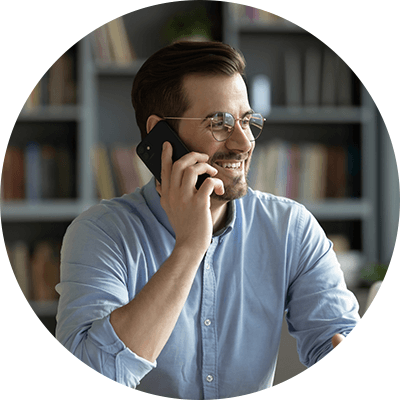 A man with brown hair and a brown beard smiling whilst on the phone.