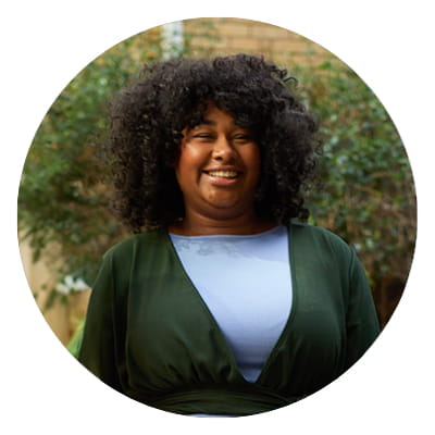 A woman with curly hair smiling wearing a green cardigan and grey top.