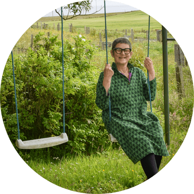 Older woman on a swing in front of countryside view.
