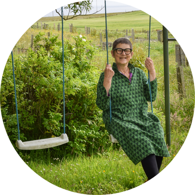 Older woman on a swing in front of countryside view.