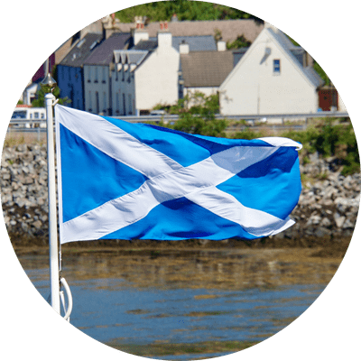 The Scottish flagging waving in the wind in front of a typical Scottish coastal town.