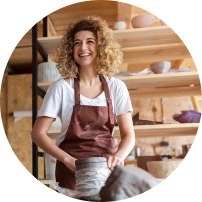 Smiling woman in brown apron working on pottery.