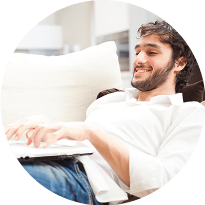 dark haired man lying on a sofa typing on a laptop
