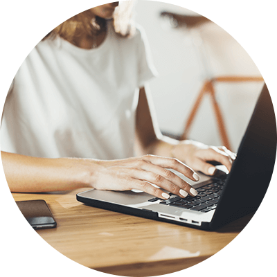 A close up of a woman typing on her laptop on a desk.