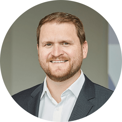 A man with short ginger hair smiling wearing a white shirt and a black suit.