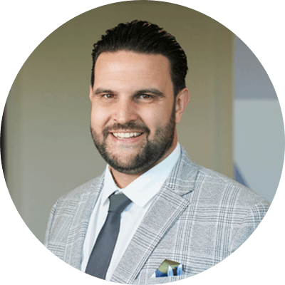 A man with short black hair and a beard smiling wearing a white and grey suit.