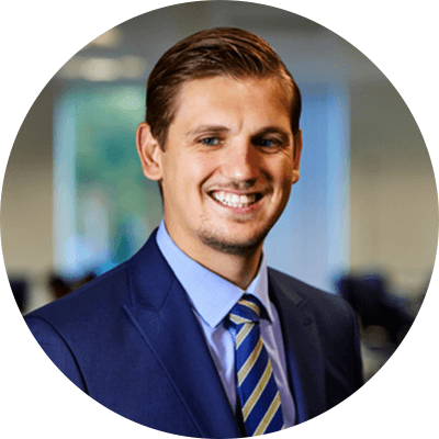 A man with short brown hair smiling wearing a blue suit with a blue shirt.