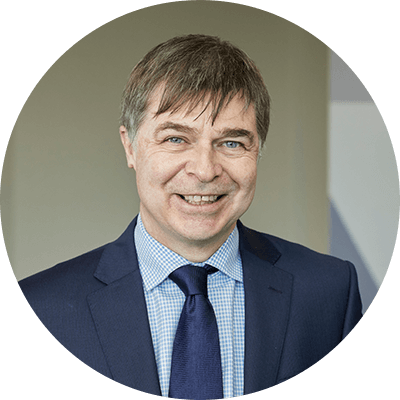 A man with short grey/brown hair smiling wearing a blue suit.