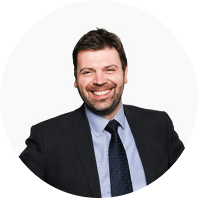 A man with short brown hair and a beard smiling wearing a black suit.