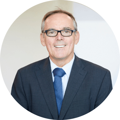 A man with short grey hair smiling wearing glasses and a blue suit.