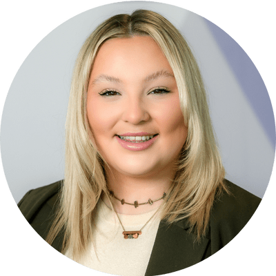 A woman with medium length blonde hair smiling wearing a white shirt and black blazer.