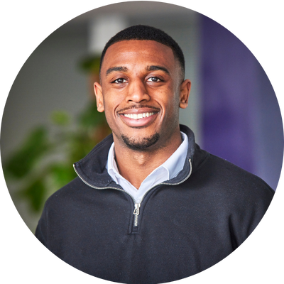 A man with short black hair smiling wearing a fleece with a shirt underneath.