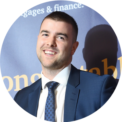 A man with short black hair smiling wearing a navy blue suit.