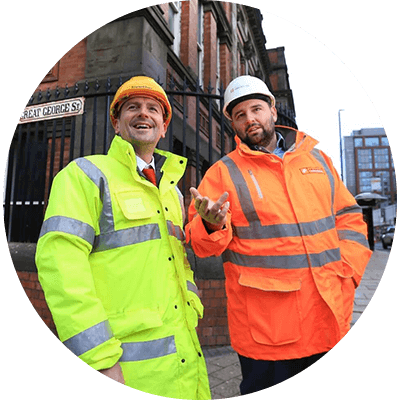 Two men in high vis talking in front of a street in Manchester.