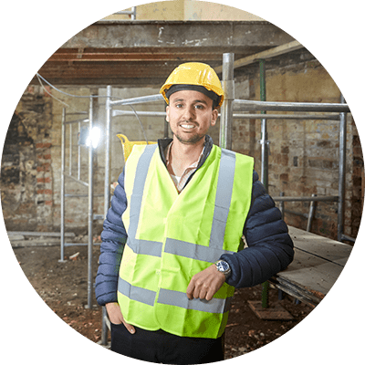 A man in a yellow high visibility vest and a hard hat on a construction site smiling and leaning on something.