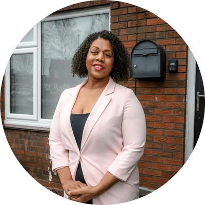 A woman stood in front of a house smiling.
