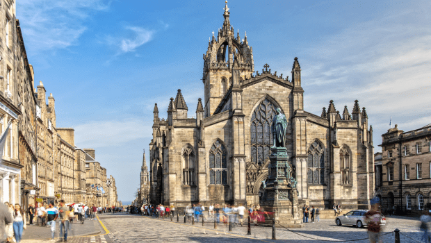 A picture of St Giles Cathedral on the busy 'Royal Mile' in Edinburgh, taken during the day with a bright blue sky and a few wispy clouds.