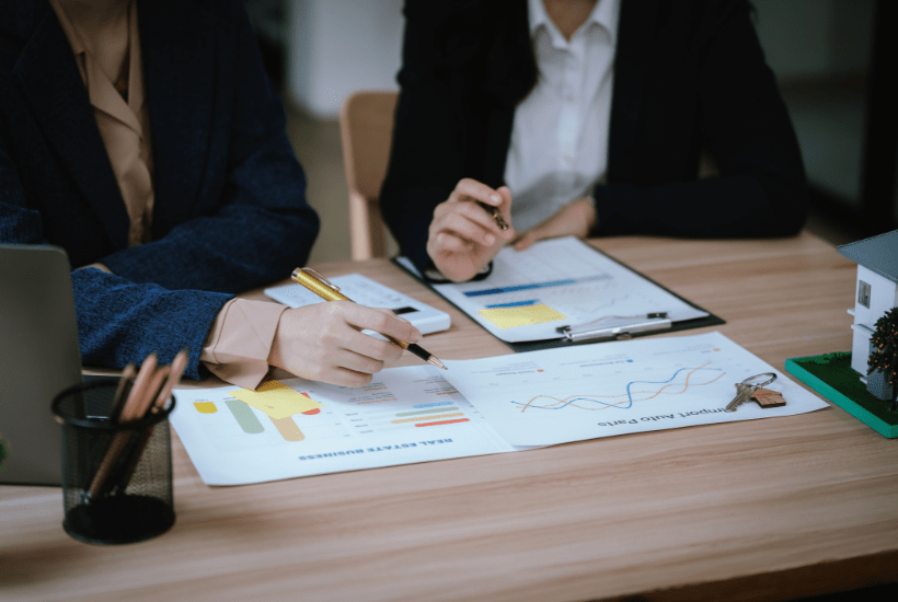 Two business women looking at real estate finances for their property portfolio on a desk.