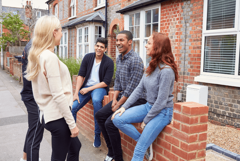 A group of happy students sat on a wall outside a house.