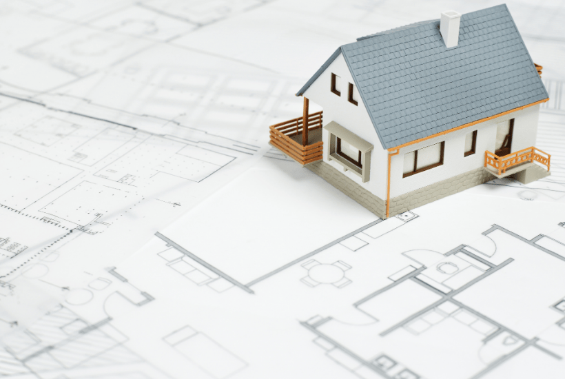 A white model house with a grey roof on top of property plans.