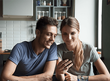 A blonde and brown haired couple both smiling at a phone screen together.