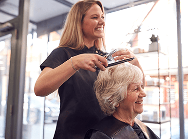 An older woman with grey hair getting her hair done by a hairdresser.