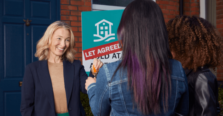 A female landlord handing over keys to two tenants.