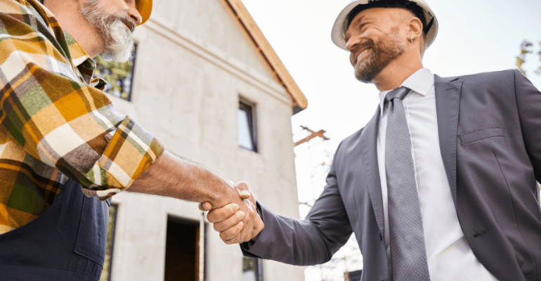 Happy builder and finance partner shaking on a housing development site.