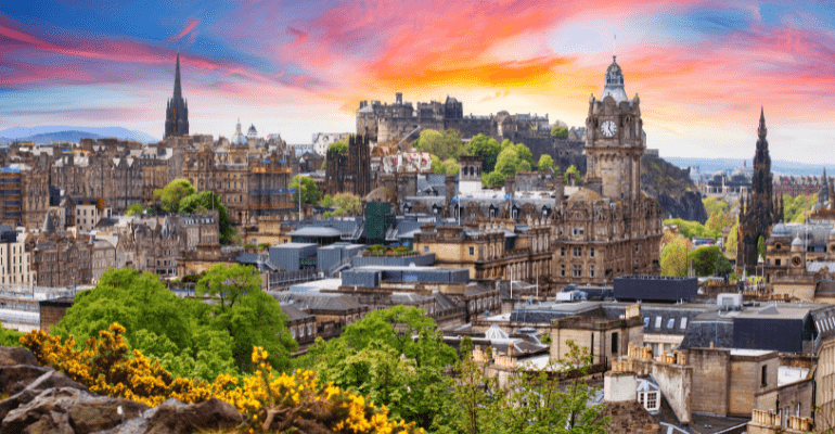 A picture of Edinburgh's skyline with a bright, colourful sunset sky of reds, pinks and blues. The image includes several landmarks with Edinburgh Castle in the background.