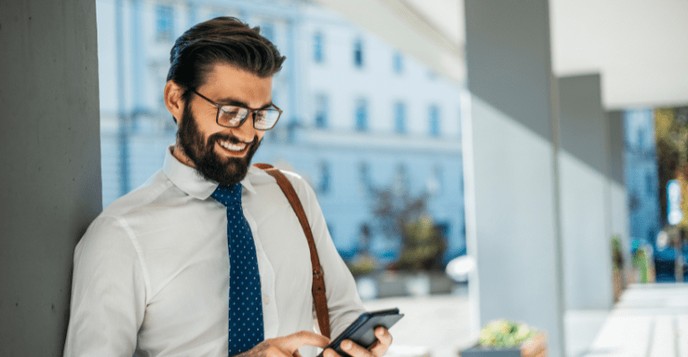 Happy young businessman with glasses and a beard looking at a phone.