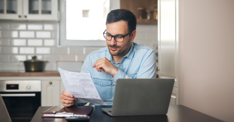 Middle-aged male landlord sat in a luxury kitchen reviewing his property portfolio.