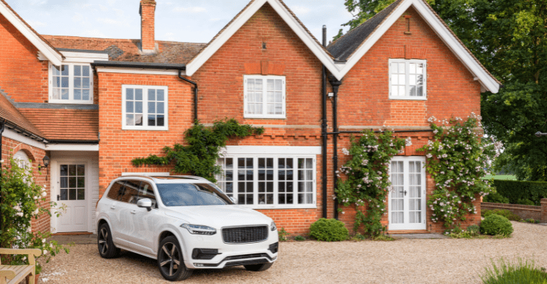 Luxury red brick country house with an expensive white SUV parked outside on a gravel driveway.