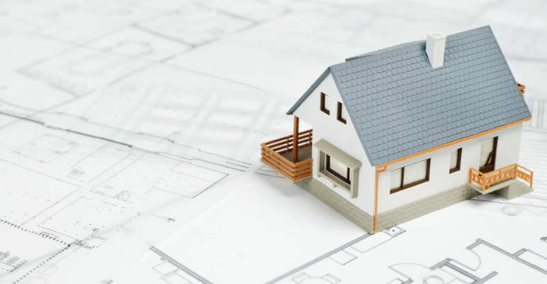 A white model house with a grey roof on top of property plans.