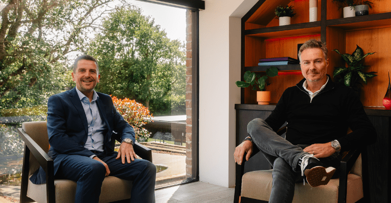 Two businessmen sitting casually in a beautiful office, smiling at the camera.
