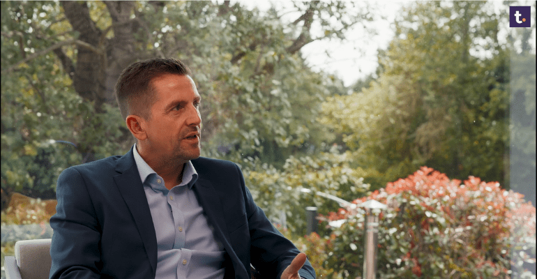 Businessman sitting in a beautiful office, talking to someone off-screen.