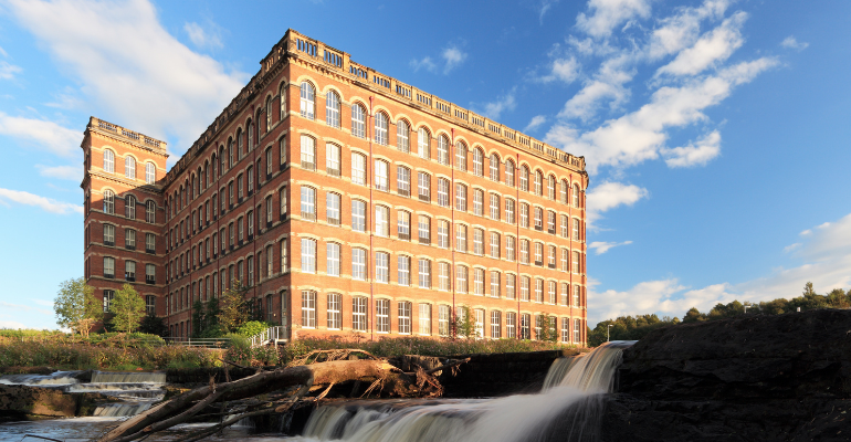 An iconic old mill building standing next to a flowing river.