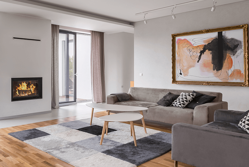 The interior of a modern house with sofas on the right, a carpet in the middle and a fireplace on the left.