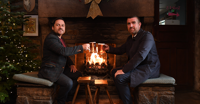 Two men sat by a fire enjoying a pint.