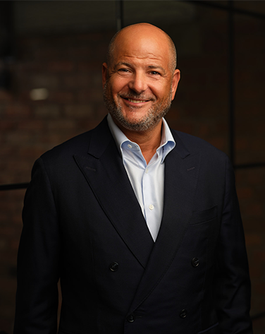 A mid shot of Marc Goldberg smiling wearing a black suit.