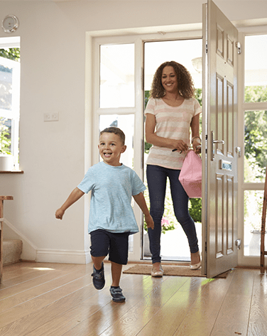 A woman and her son walking into their home smiling.