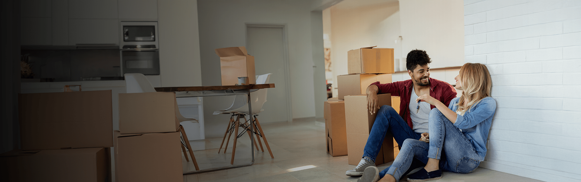 A couple sat on the floor together in their modern kitchen with moving boxes surrounding them.