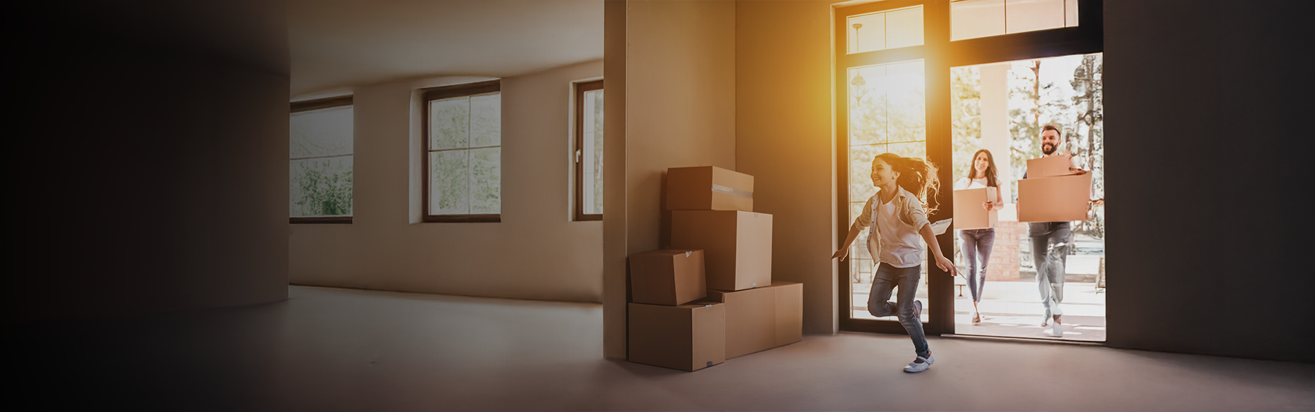 A family holding boxes moving into an empty house.