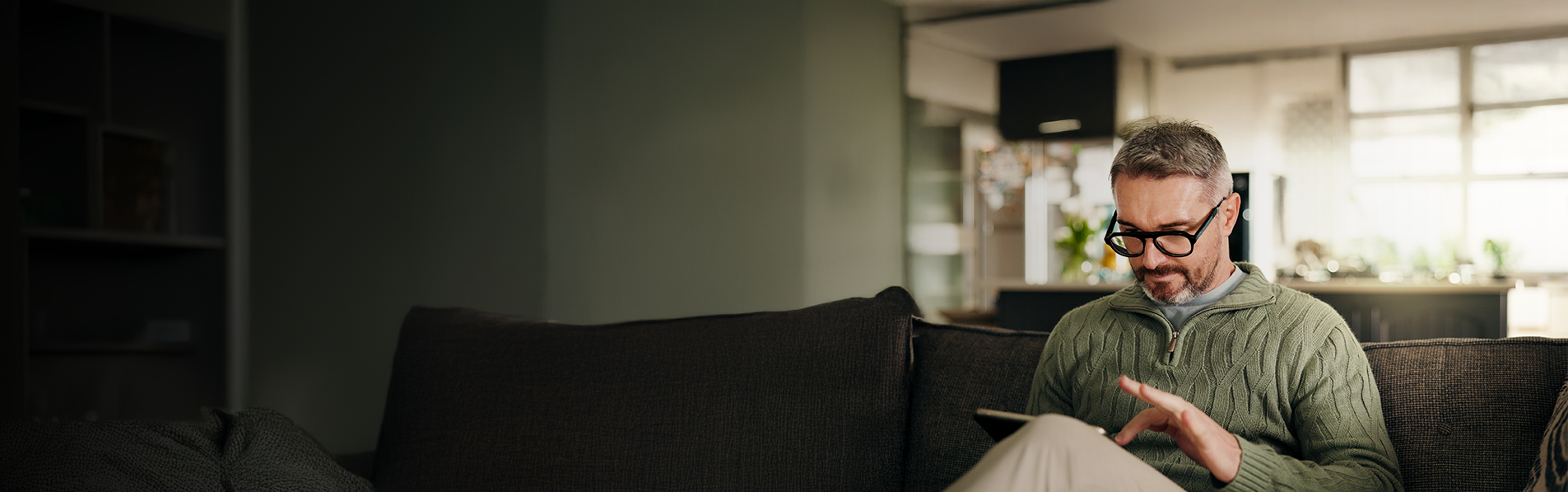 A wide shot of a older man sat on his couch using an iPad in a modern home.