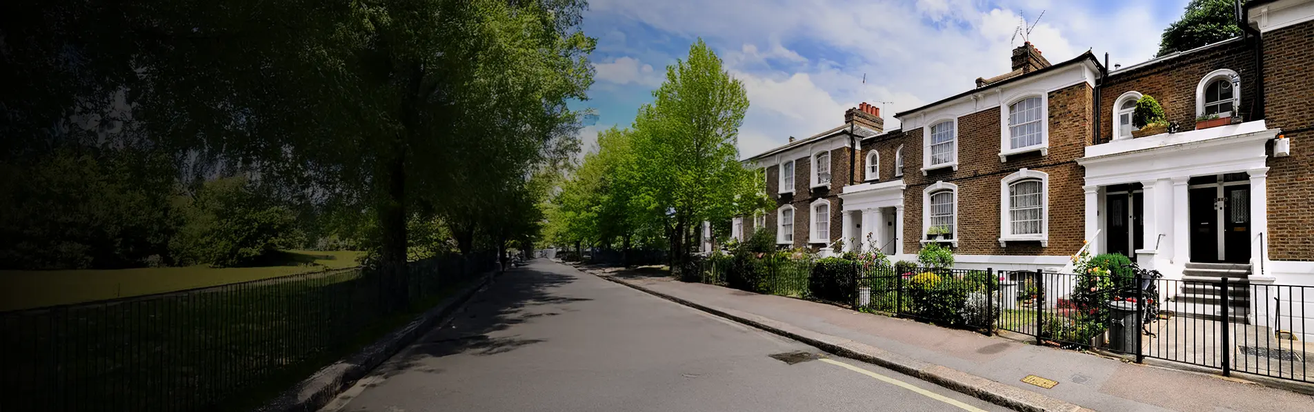 A wide shot of terraced houses on a street opposite a park.